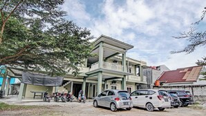 A building with a covered entrance, a parking area with several cars, and a tree in the foreground. - OYO 91642 Fhazel Residence Syariah (Pekanbaru)