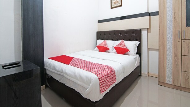 A neatly arranged bedroom with a bed, bedside table, wardrobe, and a framed picture on the wall. - OYO 91642 Fhazel Residence Syariah (Pekanbaru)