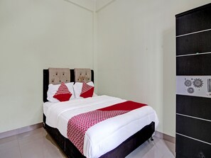 A neatly made bed with white and red bedding, a dark headboard, and a black wardrobe with a patterned door. - OYO 91642 Fhazel Residence Syariah (Pekanbaru)