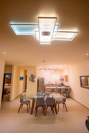 Une cuisine moderne dotée d’un îlot central, d’un coin repas avec une table en verre et d’un luminaire suspendu au plafond.
