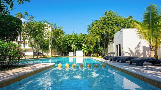 A swimming pool with clear blue water, surrounded by trees and a white building. - Luxury Apartment With Poll (Playa del Carmen)