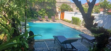 Una piscina con sillas de descanso, rodeada de vegetación y una terraza de piedra.