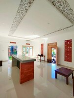 Una habitación amplia con un mostrador de recepción de madera en el centro, suelo de baldosas y techo con diseño.