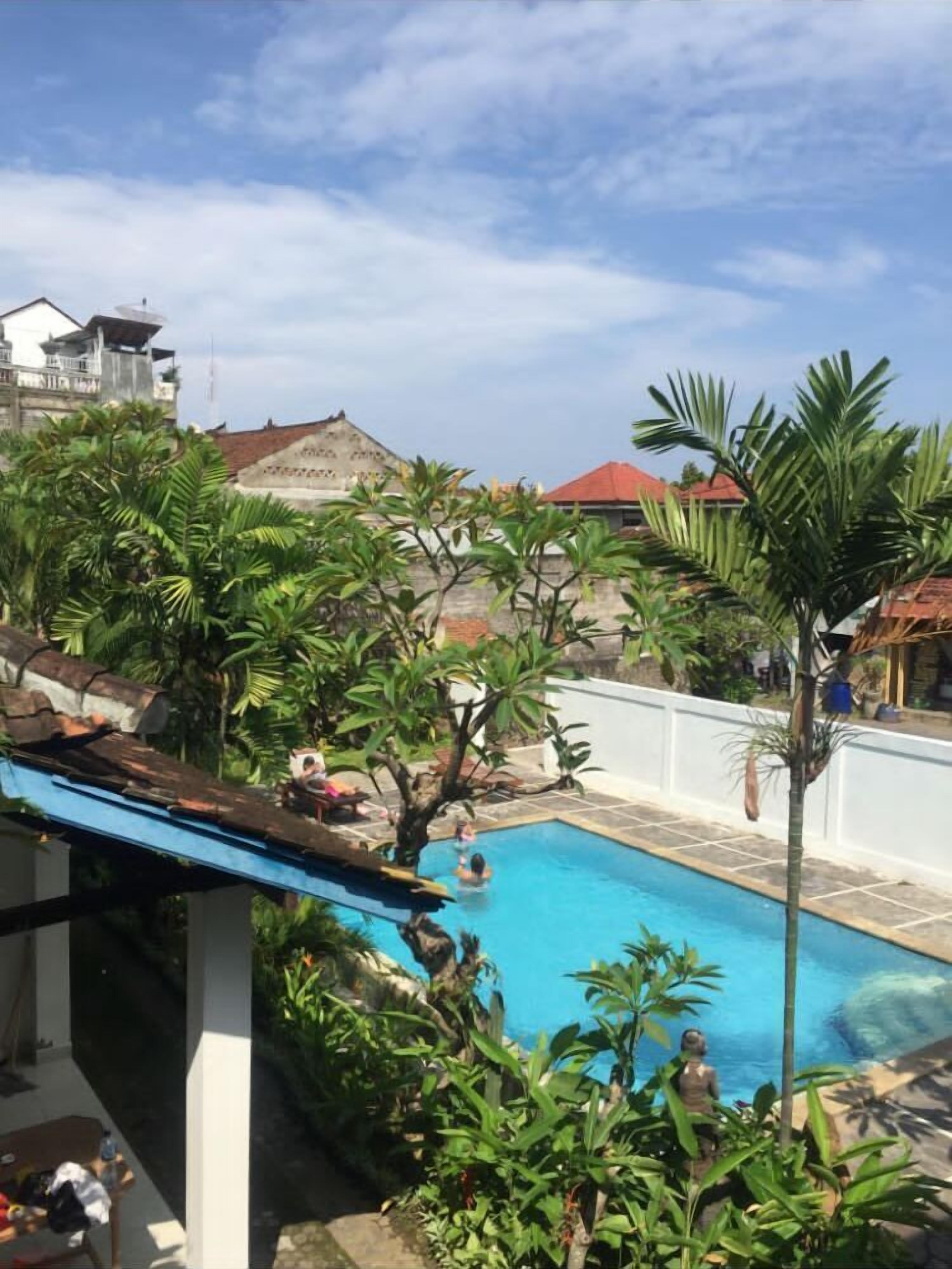 Una piscina rodeada de abundante vegetación y una valla blanca.