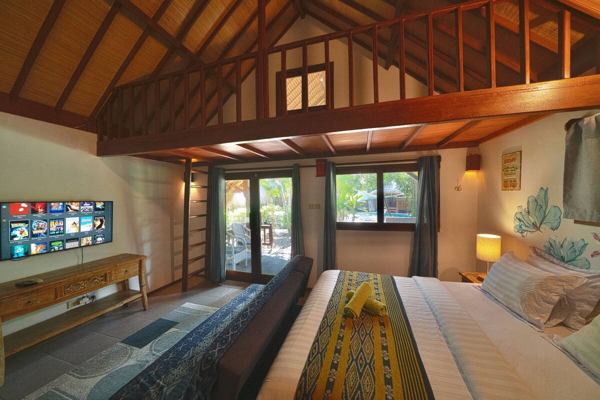 Une chambre d’hôtel avec un grand lit, un banc en bois, un téléviseur fixé au mur et un balcon donnant sur l’extérieur.