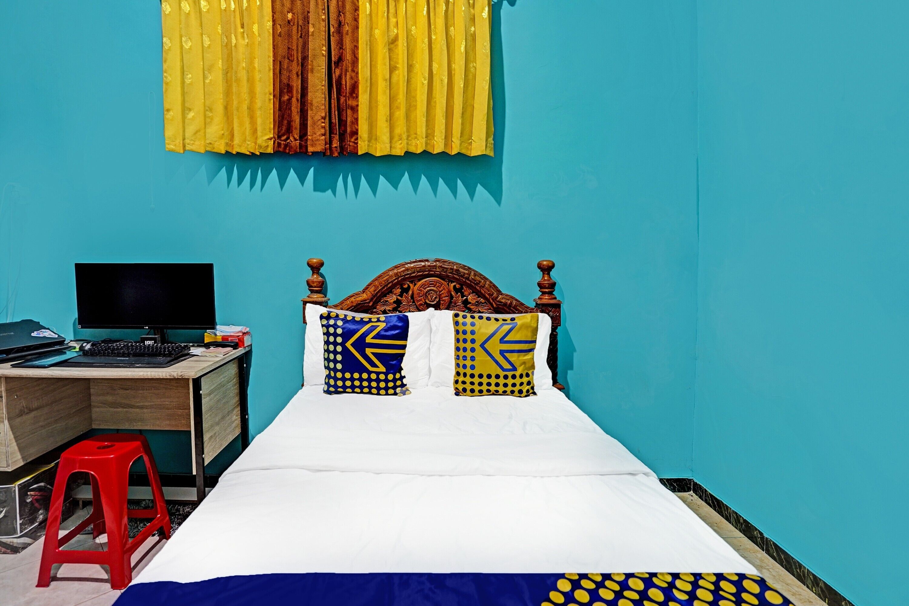 A bedroom with a bed, a desk with a computer, and a red stool.