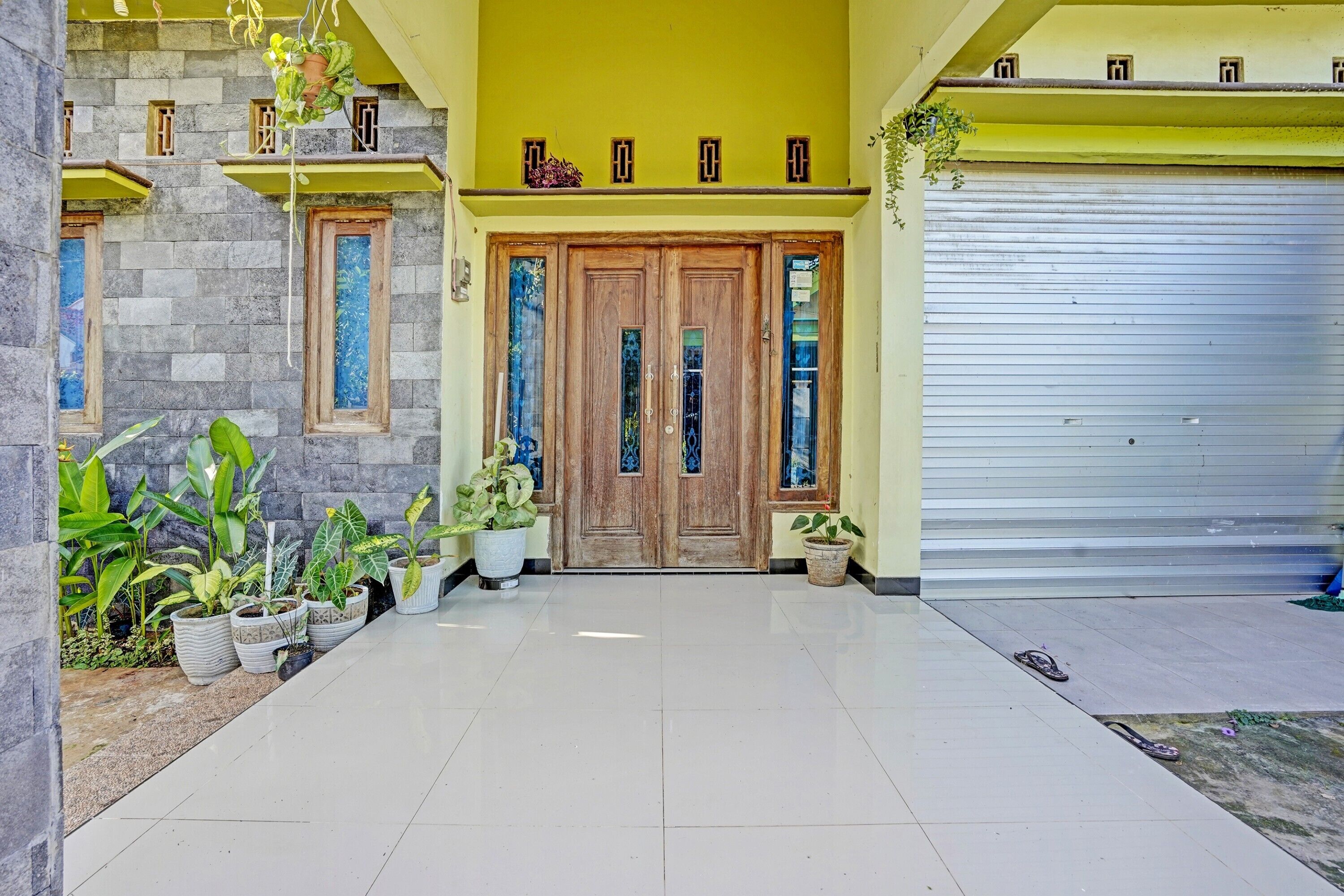A clean, tiled entrance with a wooden double door, potted plants, and a garage door.