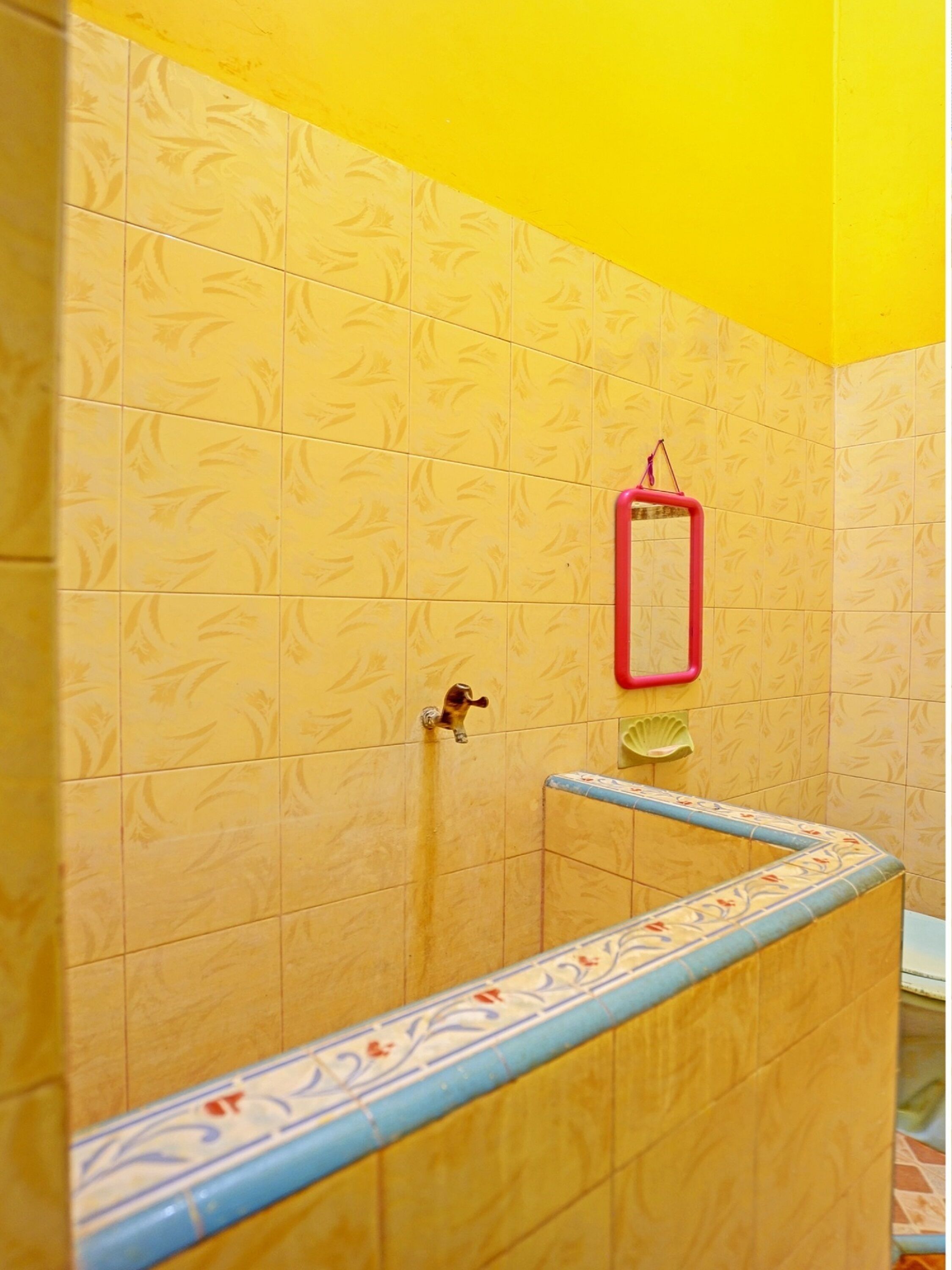 A bathroom with yellow patterned tiles, a red towel rack, and a blue-tiled shower area.