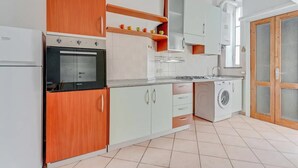 A modern kitchen with wooden cabinets, a built-in oven, a washing machine, and a sink. - ITS HOME VIA MODICA (Milano)