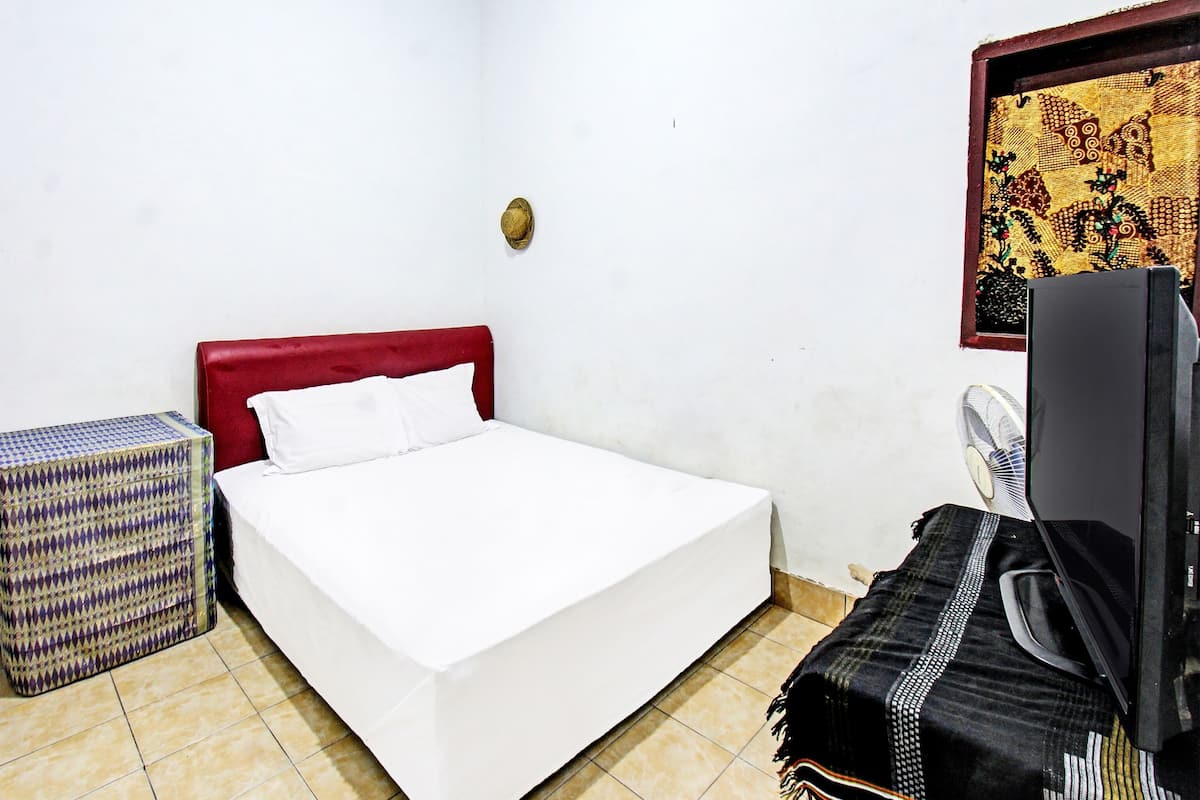 Una habitación con cama, una mesita, televisor y un adorno en la pared.