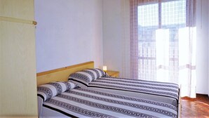Une chambre à coucher avec un lit, une tête de lit en bois, une table de chevet et une fenêtre avec un rideau.