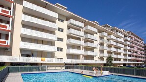 Un immeuble résidentiel à plusieurs étages, doté de balcons, d’une piscine et surplombant un ciel d’un bleu limpide.