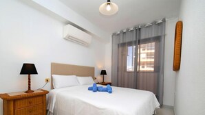 Een hotelkamer met een bed, twee nachtkastjes, een lamp, een airconditioning en een raam met gordijnen.