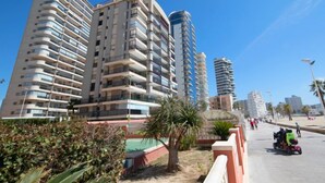 Een modern hoogbouwgebouw met meerdere balkons, een verharde looppad en palmbomen.