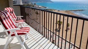 Een balkon met twee gestreepte stoelen, uitzicht op een strand en een berg in de verte.