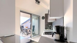 Eine moderne Küche mit Einbauherd, Kaffeemaschine und einer Schiebetür zu einem Sitzbereich im Freien.