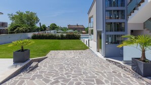 Ein modernes Gebäude mit einer gepflasterten Terrasse, einem kleinen Rasen und Kübelpflanzen.