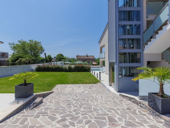 Un edificio moderno con un patio empedrado de piedra, un pequeño césped y plantas en macetas.