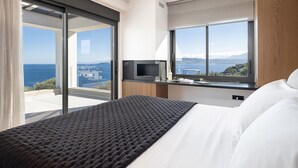 A modern hotel room with a large bed, a television, and a view of the sea. - Stunning sea views, heated pool, fire pit, child pool: by etouri (Chania)