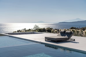 A pool with a lounge chair and a view of the sea.