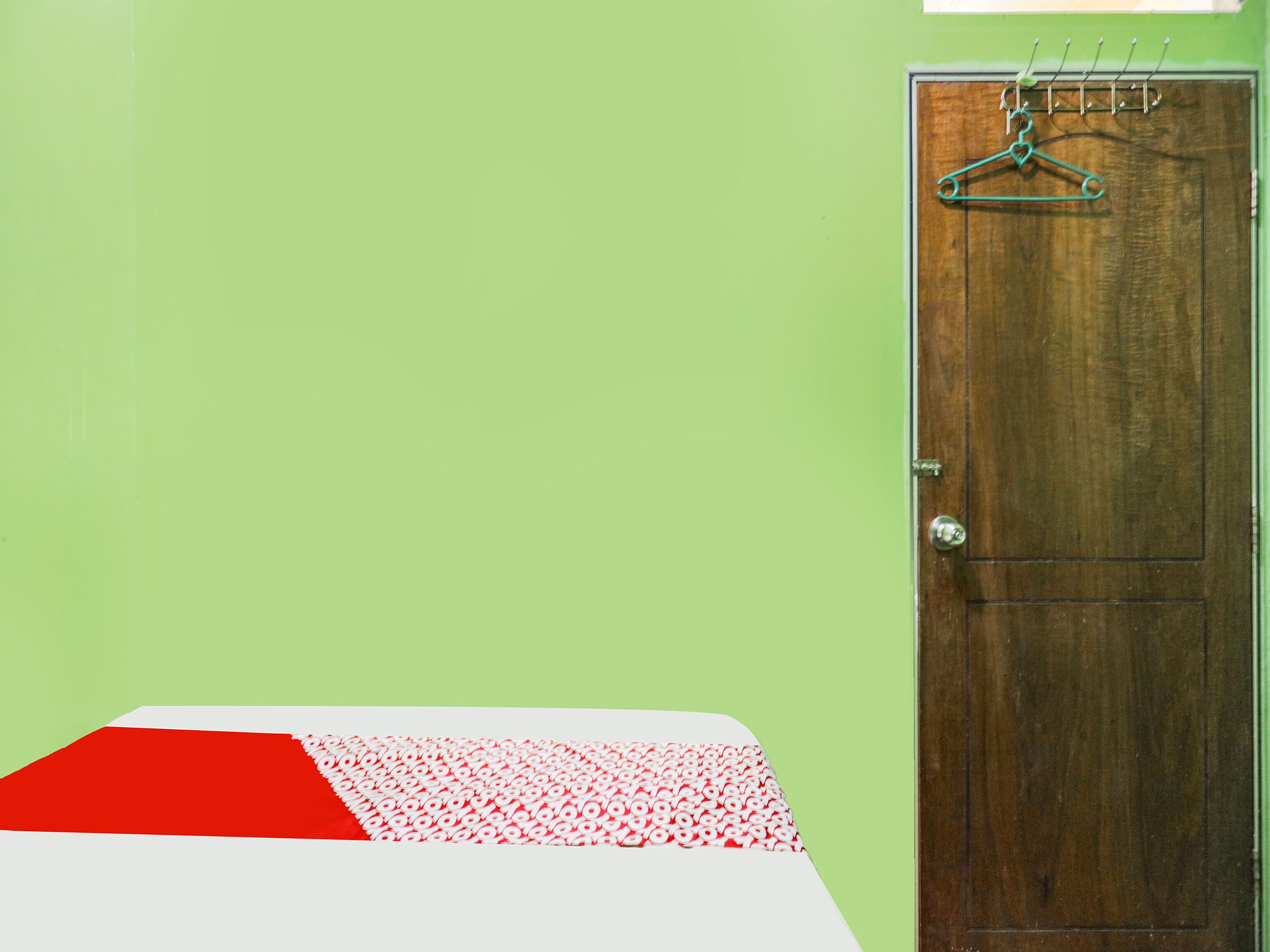 A room with a wooden door, a bed with a red and white bedspread, and a green wall.