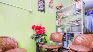 A room with green walls, wicker chairs, a table with a vase of flowers, and shelves with kitchenware. - Hotel O Bilqis Homestay NearThe Hot River, Dog Run (Batam)