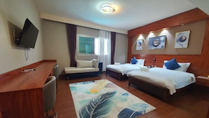 Habitació d'hotel amb escriptori de fusta, dos llits, televisió i obra d'art a la paret.