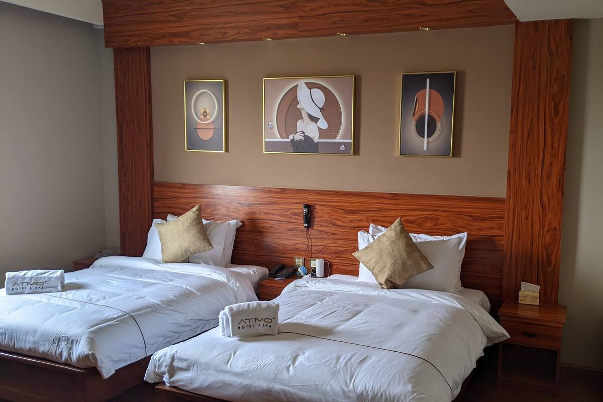 A hotel room with two beds, wooden headboard, and three framed artworks on the wall.