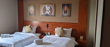 Une chambre d’hôtel avec deux lits, une tête de lit en bois et trois œuvres d’art encadrées accrochées au mur.