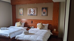 Una habitación de hotel con dos camas, cabecera de madera y tres cuadros enmarcados en la pared.
