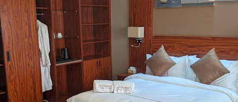 A hotel room with a wooden wardrobe, a bed with white linens, a bench, and a striped rug.
