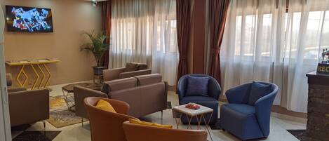 A modern living room with a flat-screen TV, comfortable seating, and a large window with curtains.