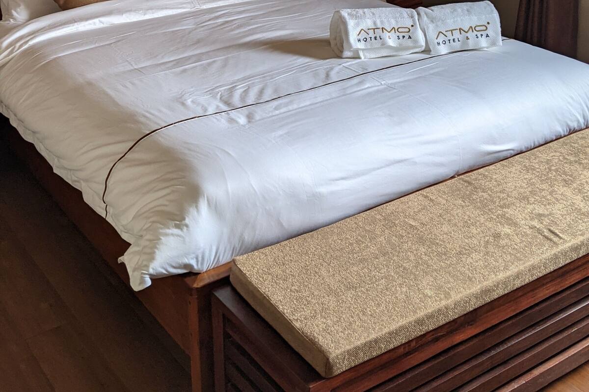 A neatly made bed with a white comforter and a folded towel with the logo 'ATMO HOTEL & SPA'.
