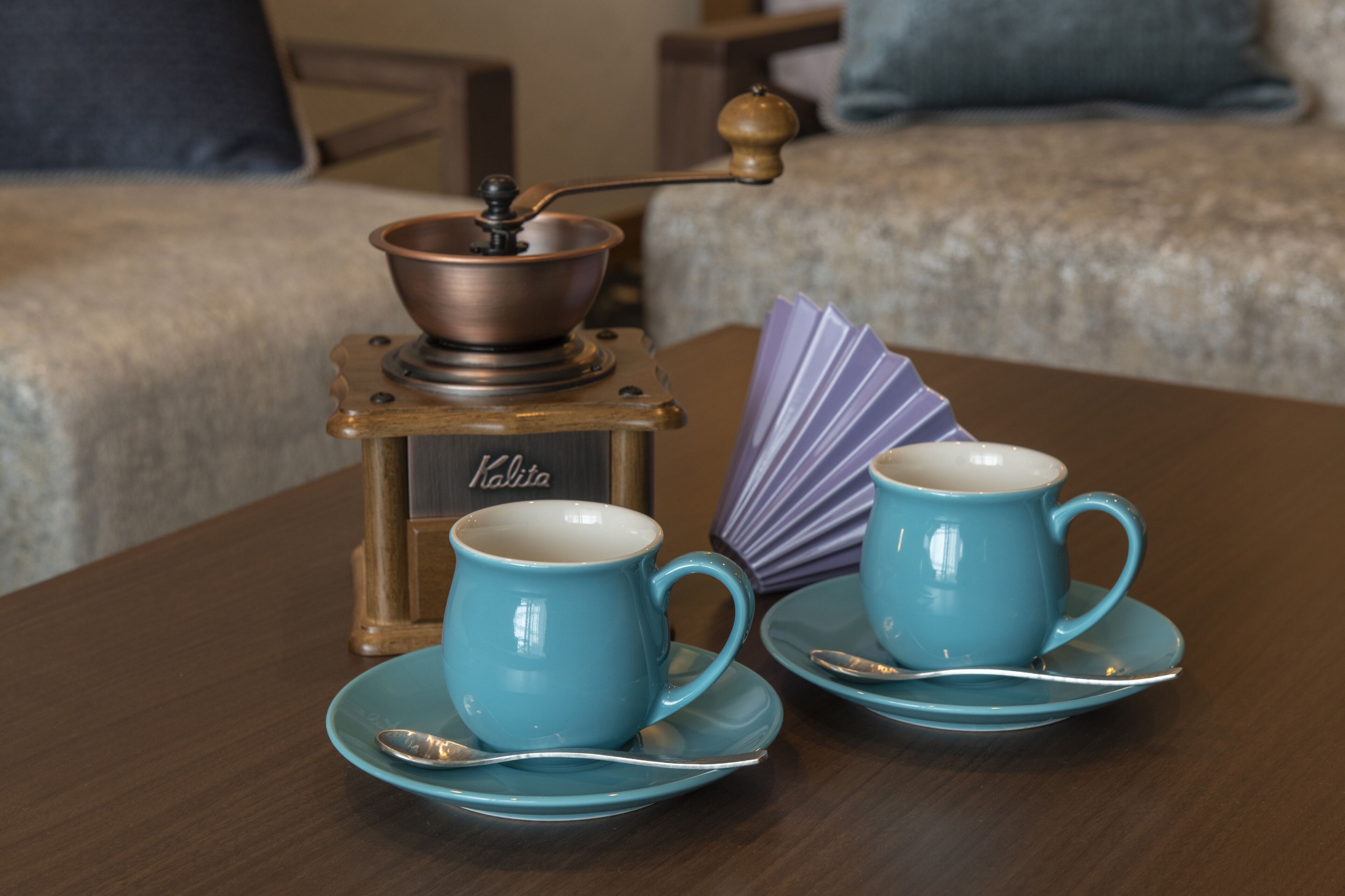 A coffee maker on a table with two blue cups and saucers.