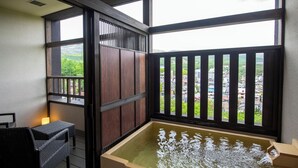 Una habitación con suelo de estera de tatami, puerta corredera de madera, mesa de tatami, banco de tatami y un ventanal con vistas a un paisaje urbano.