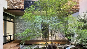 Un espacio exterior moderno con un muro de piedra, una terraza de madera y un pequeño elemento acuático.