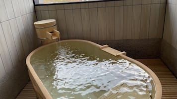 A hot tub with a wooden interior and a view of mountains through a window.