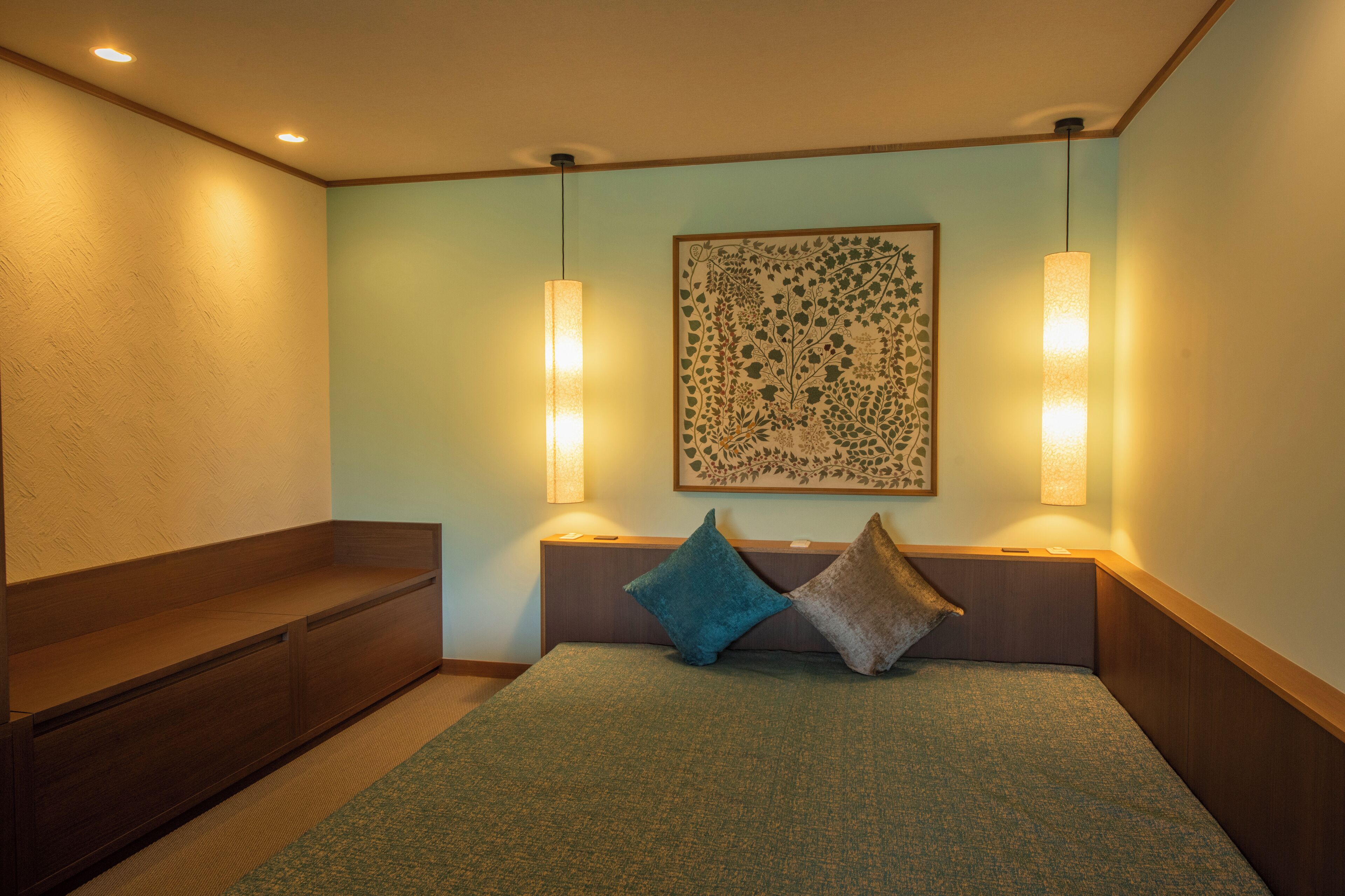 A hotel room with a bed, bedside lamps, a wall-mounted artwork, and a wooden bench.