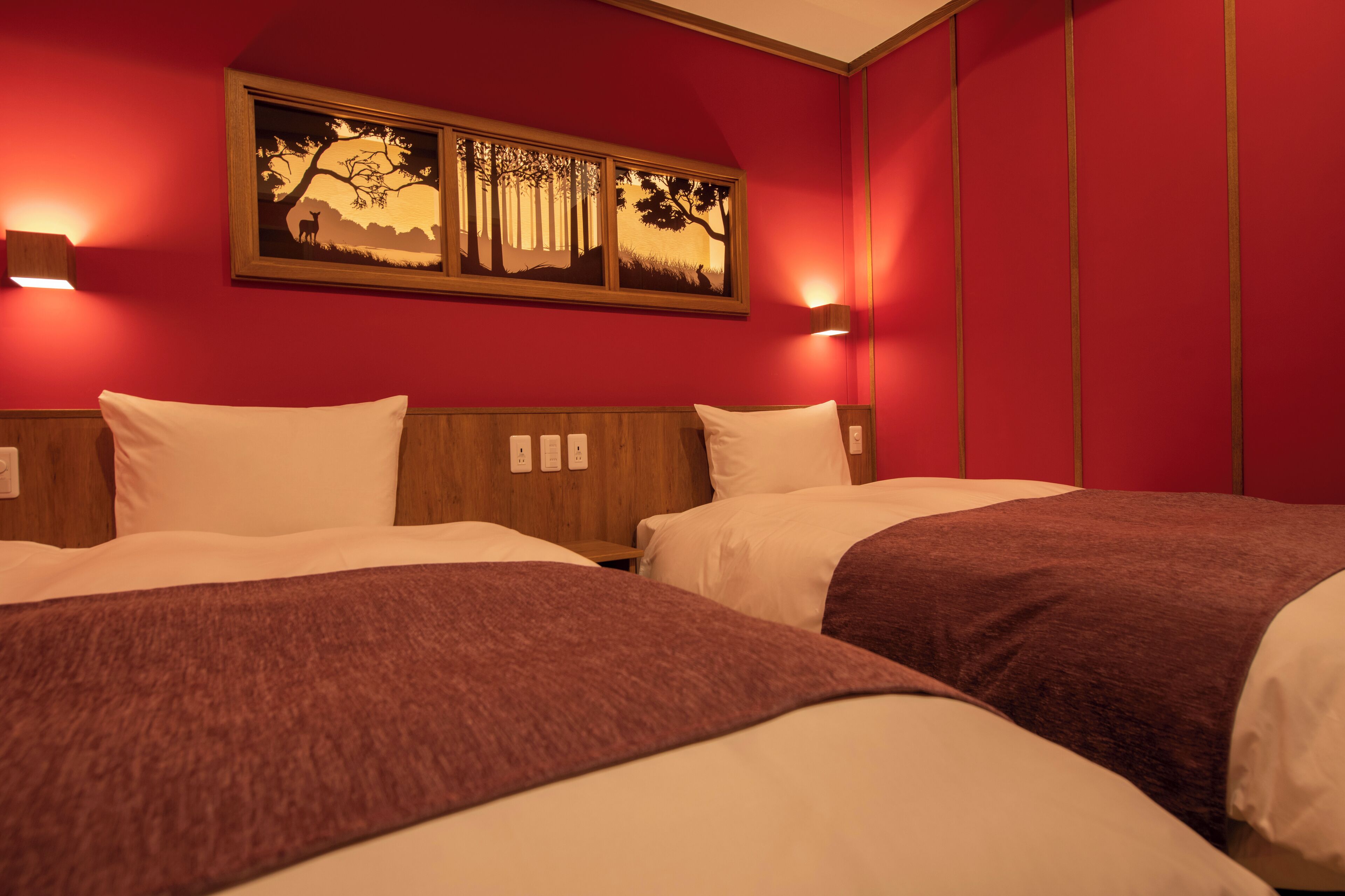 A hotel room with two beds, red walls, and a painting above the beds.
