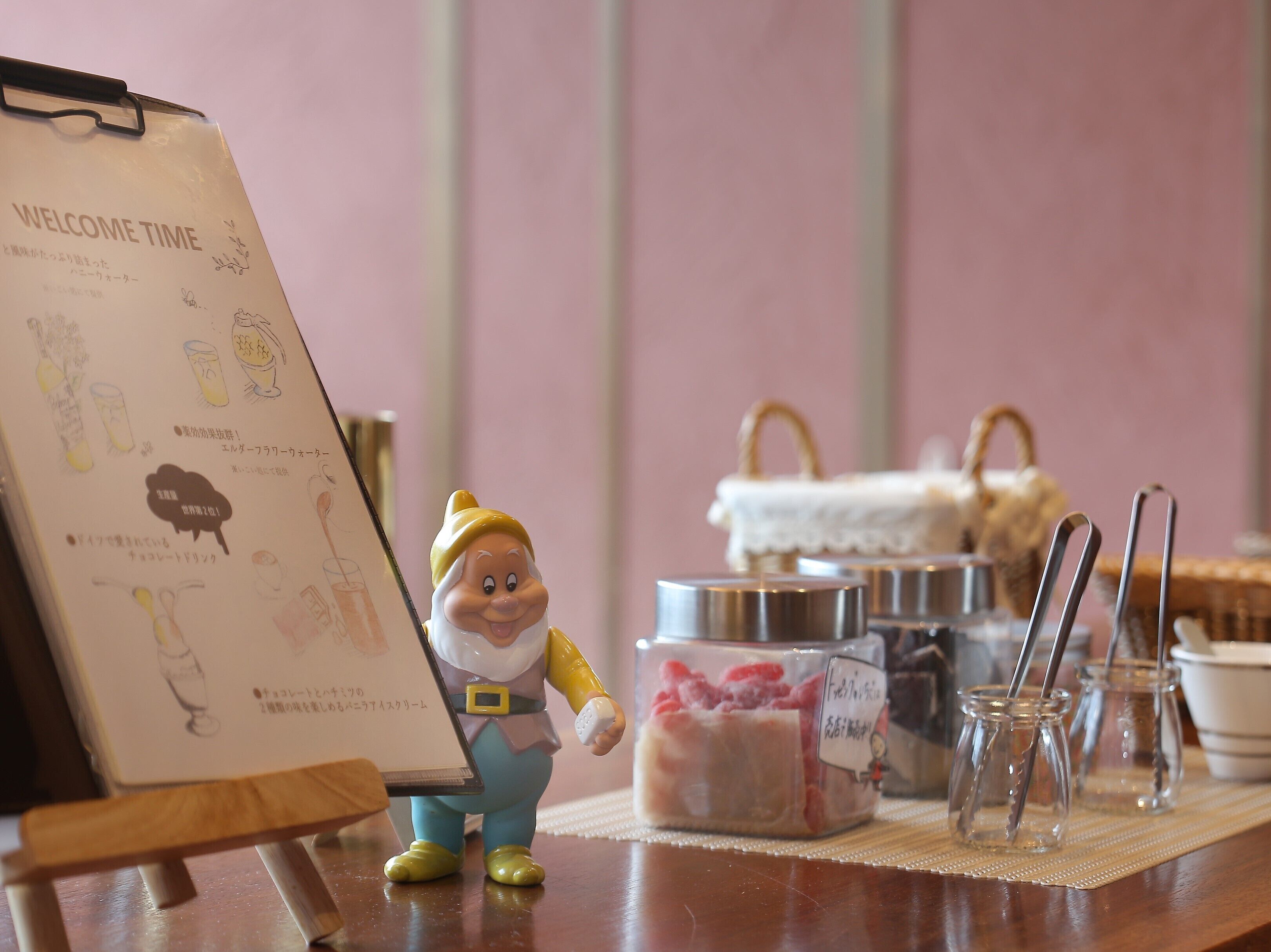 A figurine of a character standing next to a clipboard with a menu, jars of food, and a basket in the background.