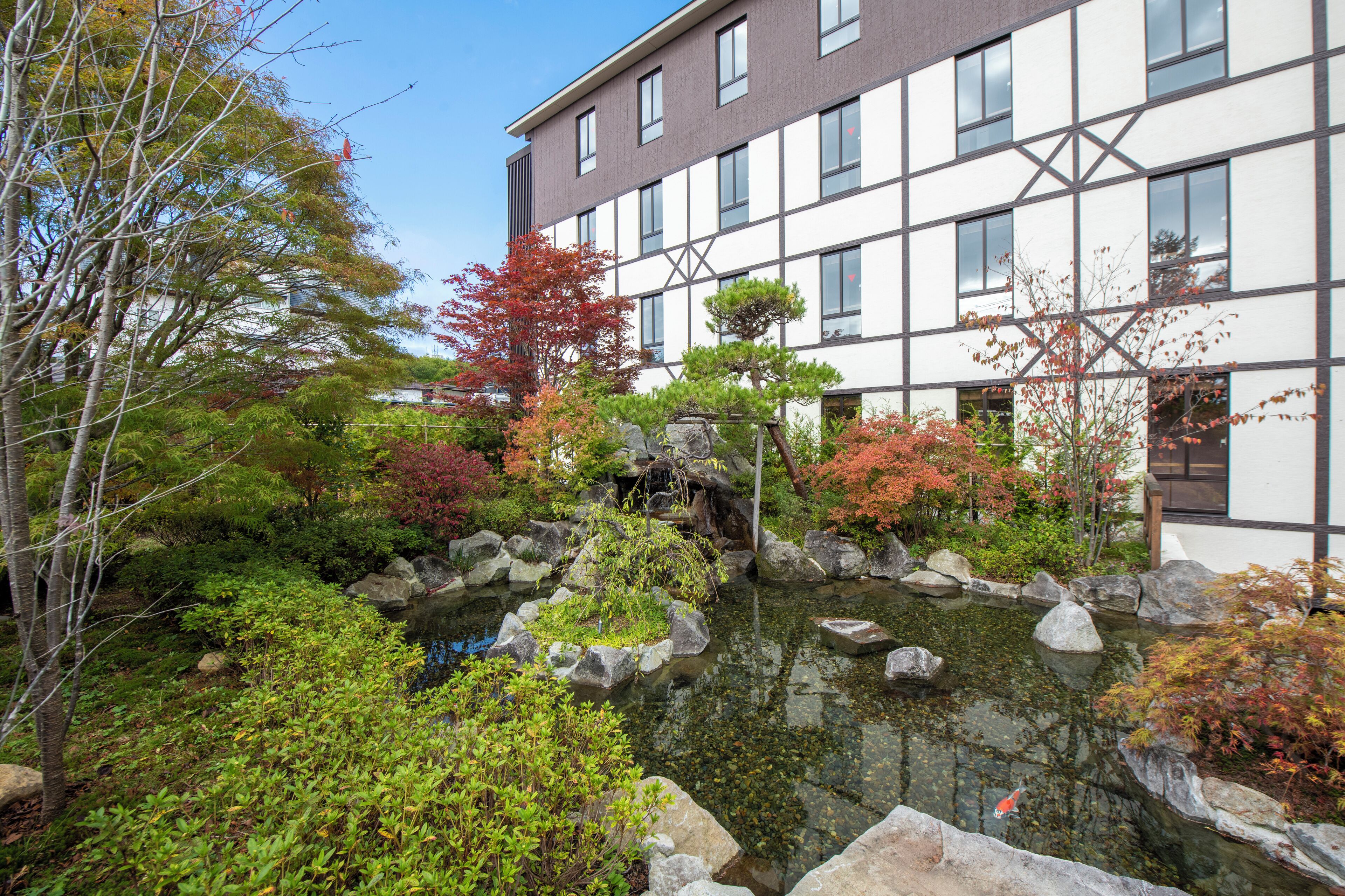 Un edificio con un jardín tradicional japonés al frente, que incluye un estanque y rocas.
