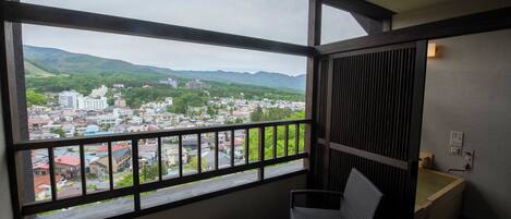 A balcony with a view of a cityscape and mountains. There are two wicker chairs and a small table.