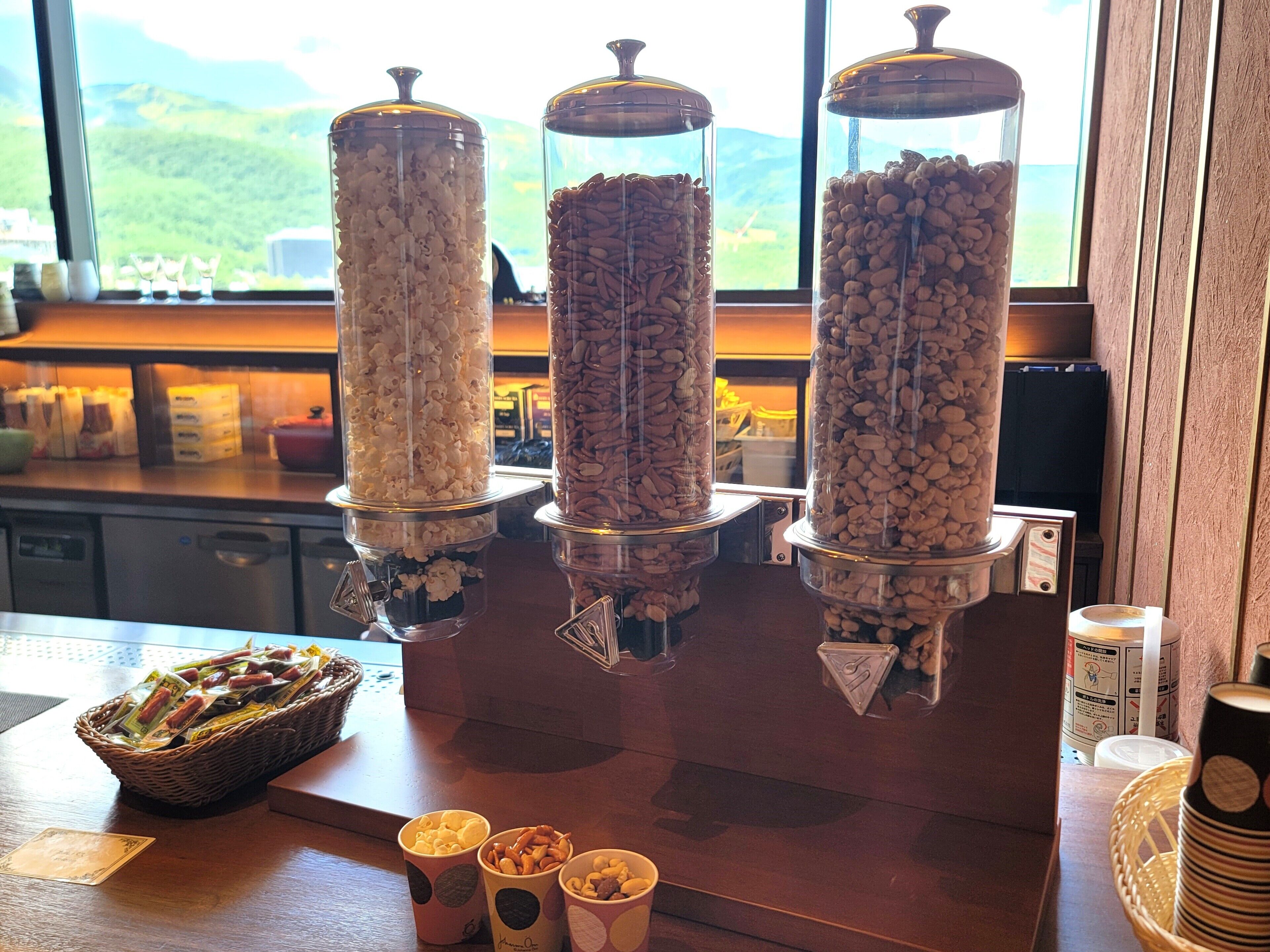 Three glass dispensers filled with popcorn and nuts on a counter.