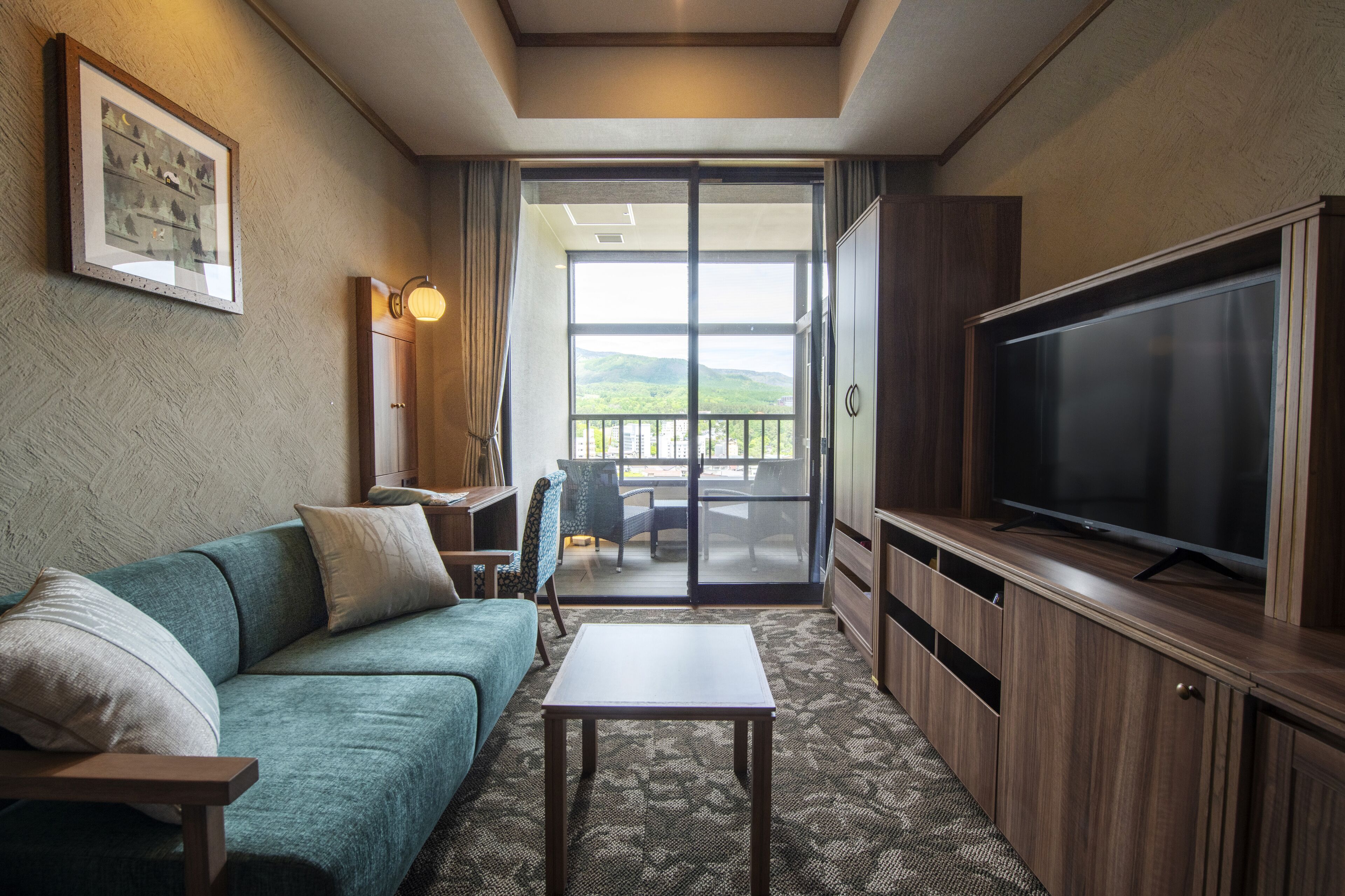 A living room with a sofa, a table, a TV, and a balcony with a view.