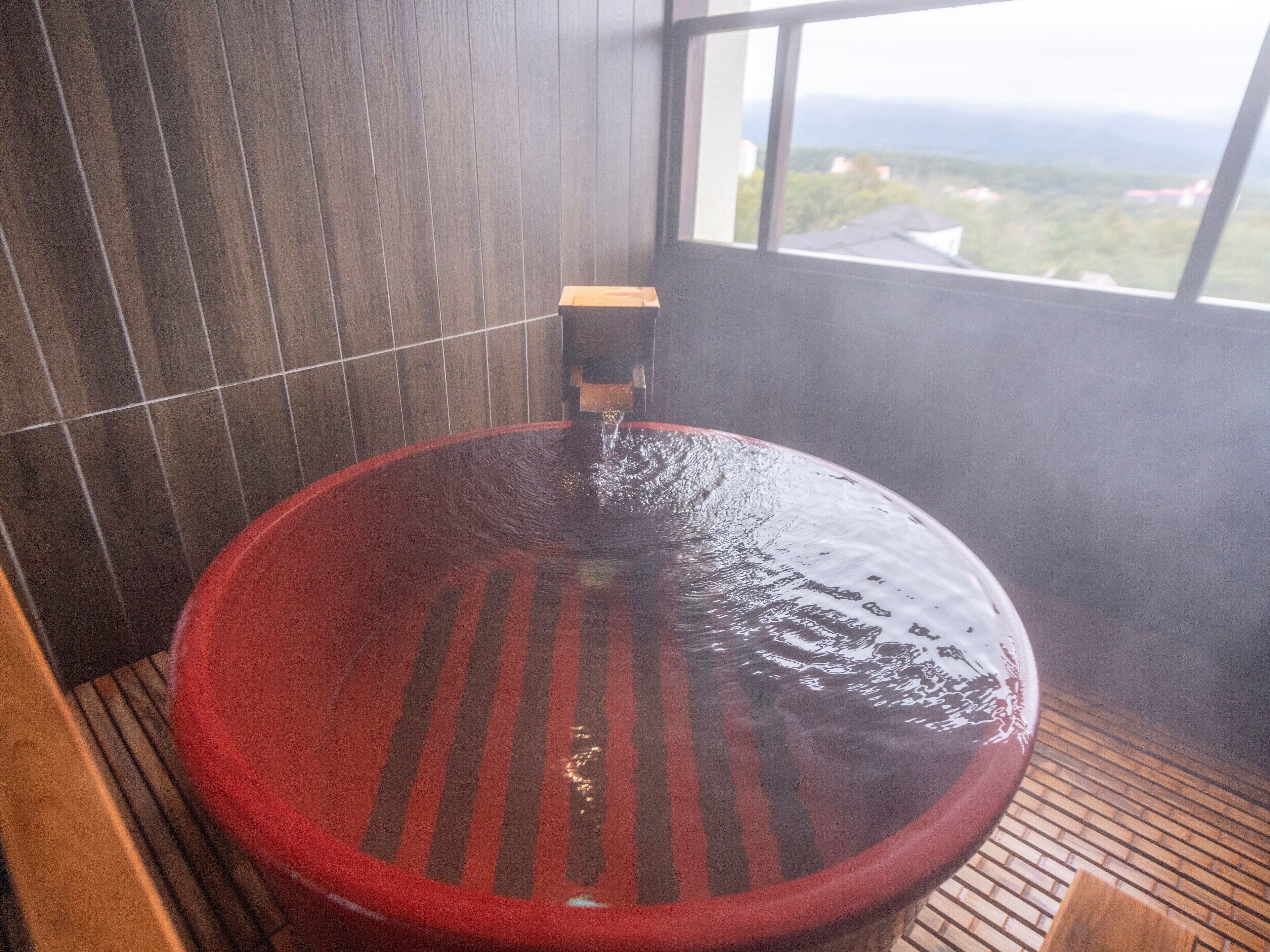 Un jacuzzi con un banco de madera, una pared con azulejos y una ventana con vistas al paisaje.