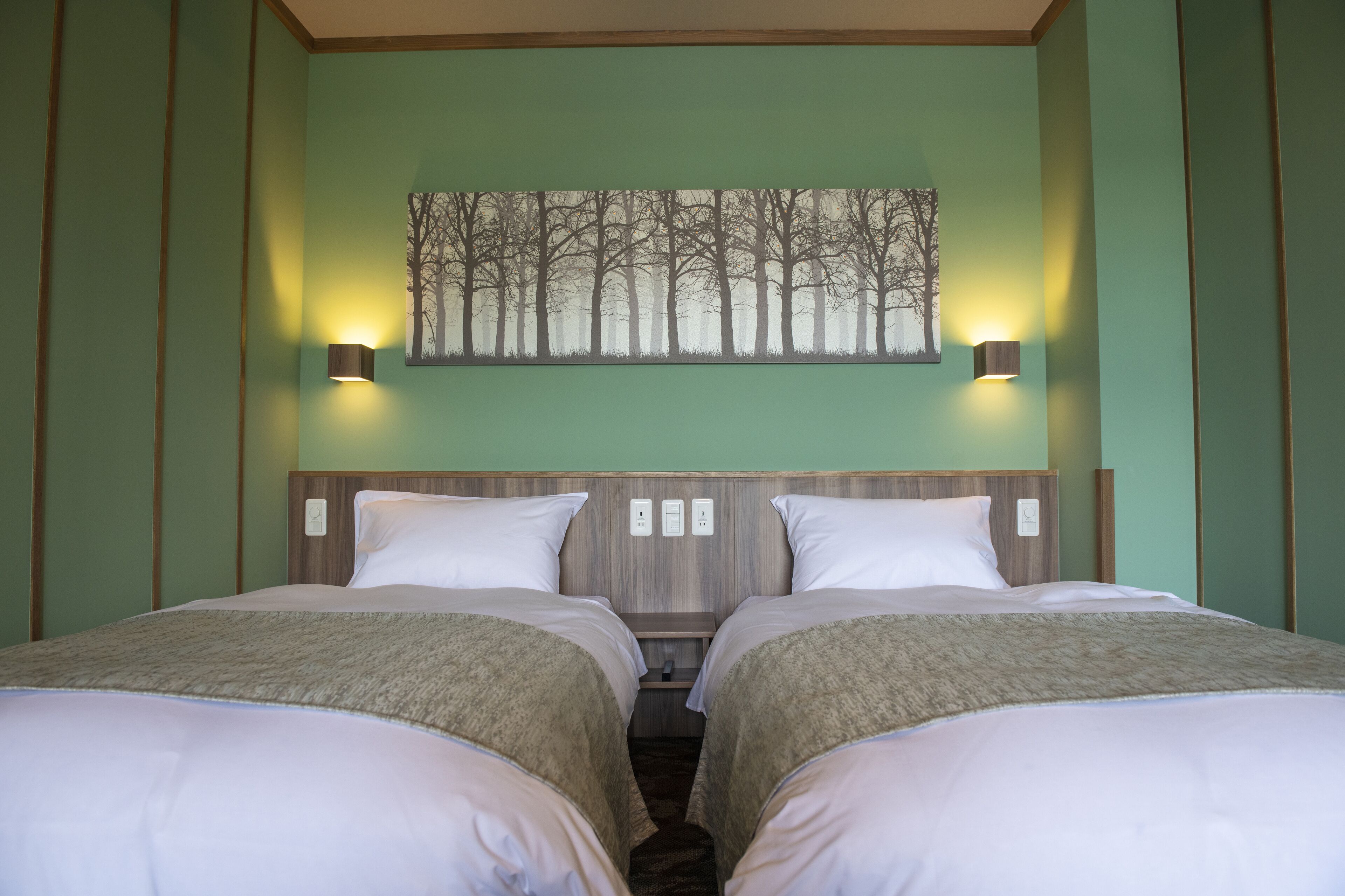 A double room with two beds, a headboard with a light switch, and a wall-mounted painting of trees.