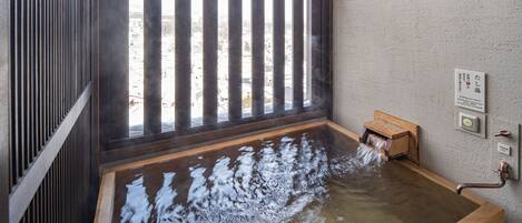 A hot spring bath with wooden railings and a wooden box for washing.
