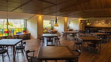 Un comedor amplio con varias mesas y sillas, ventanas grandes con vistas a zonas verdes y estanterías coloridas con libros infantiles.