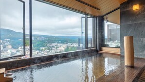 Baño de aguas termales con vistas a un paisaje urbano a través de amplias ventanas.
