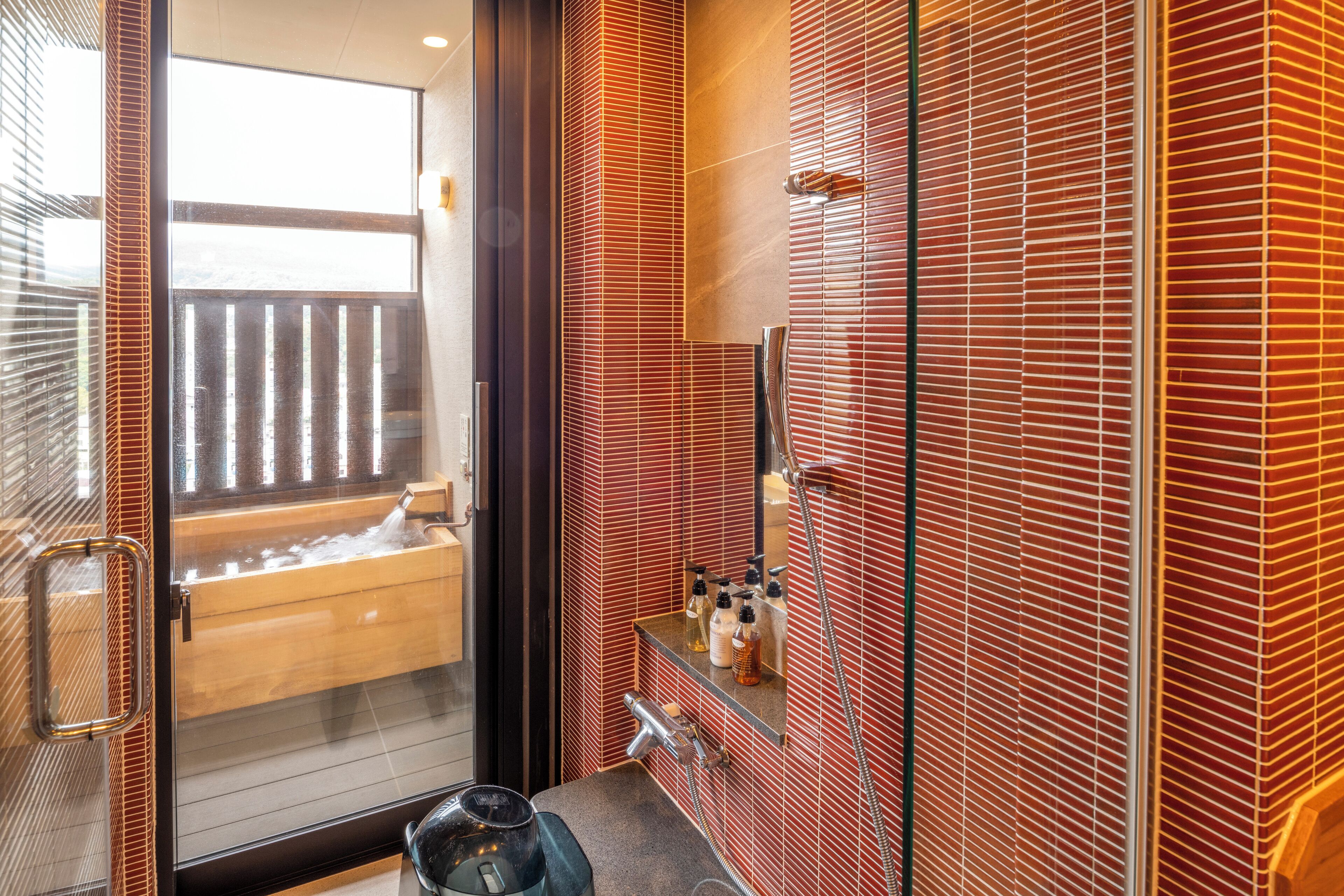 Een moderne badkamer met een houten bad, een glazen douchecabine en een rode tegelwand.